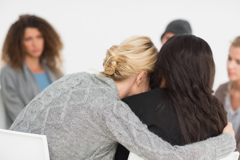 Women embracing in rehab group at therapy session in library