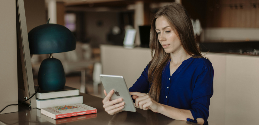 A woman seated at a desk reads on an iPad.