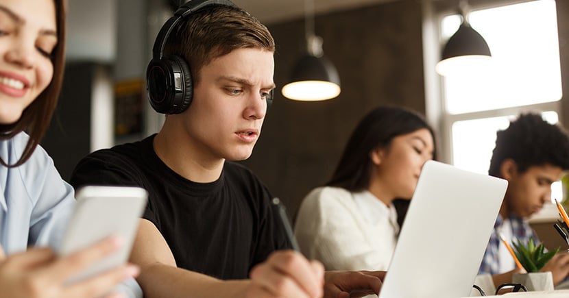 Student in a library with headphones and working with its computer